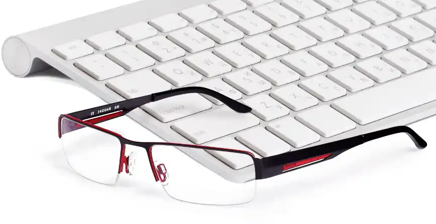Brille mit schwarz rotem Gestell liegt vor einer Tastatur auf dem Schreibtisch
